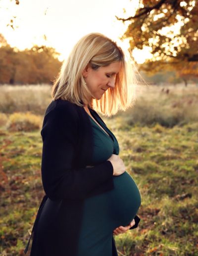 Maternity photographer REading - pregnant women looking at her tummy and smiling in beautiful autumn day