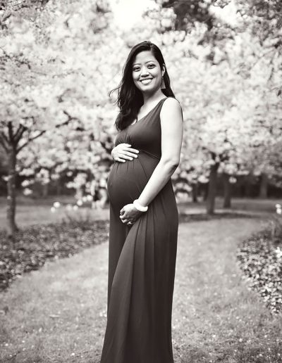 Ania Chandra maternity Photographer. Beautiful black and white photo of pregnant women in long dress holding her tommy and smiling. Background of beautiful flowers