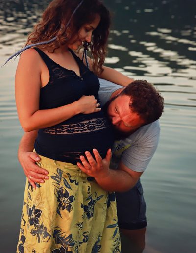 Ania Chandra maternity photographer in Berkshire and beyond. Pregnant mama is standing in the water and her husband is next to her cuddling up her tommy and kissing her belly :)