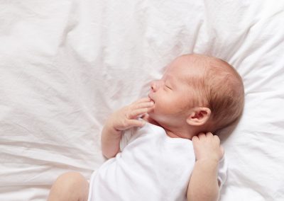 Newborn baby lying on white sheet looking very natural and cute - Ania Chandra photography Berkshire