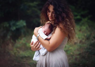 ania chandra photographer in reading - newborn baby is held by mum on her chest in beautiful green forest